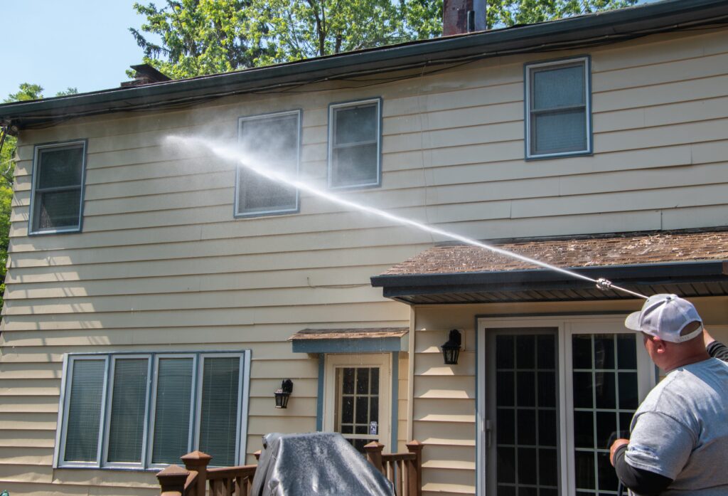 guy soft washing the siding of a house